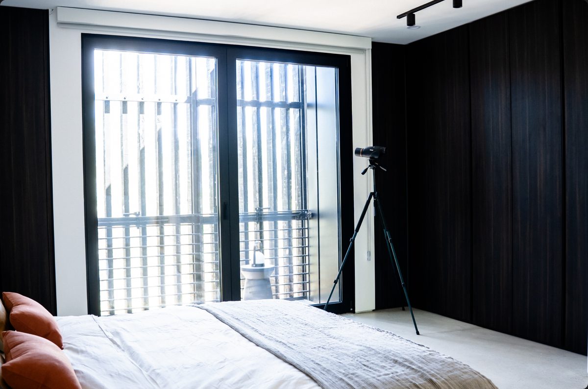 A bedroom in a finished HOWMZ home with full-height glazing and dark timber walls